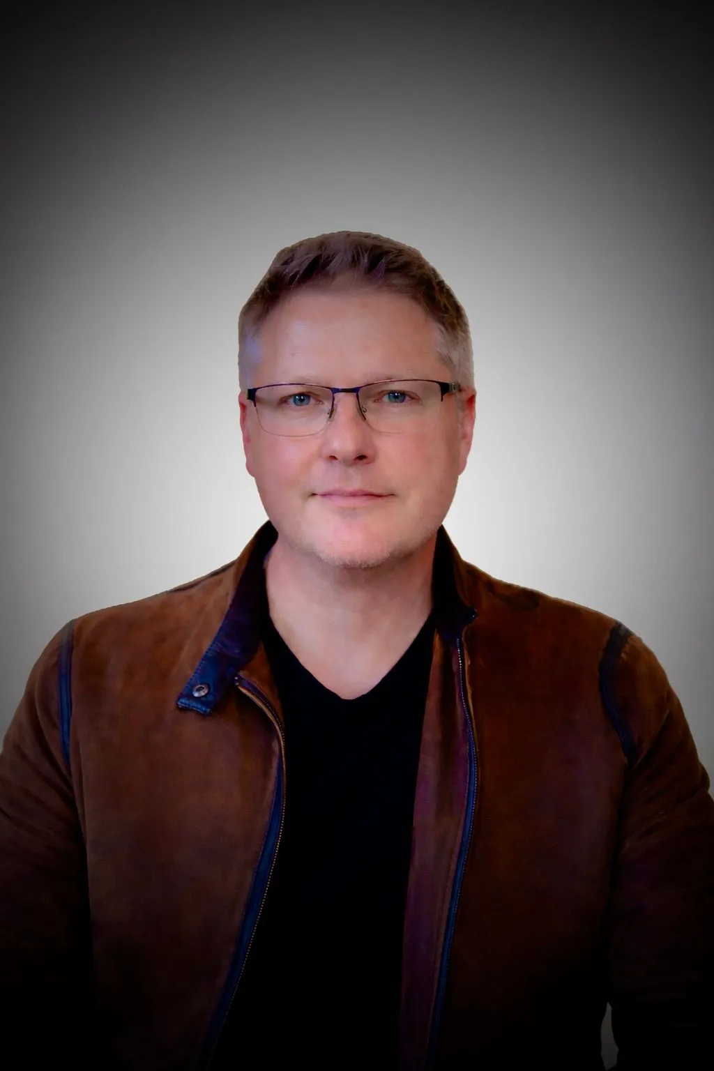 Portrait of Glenn Bauman wearing glasses and a brown jacket